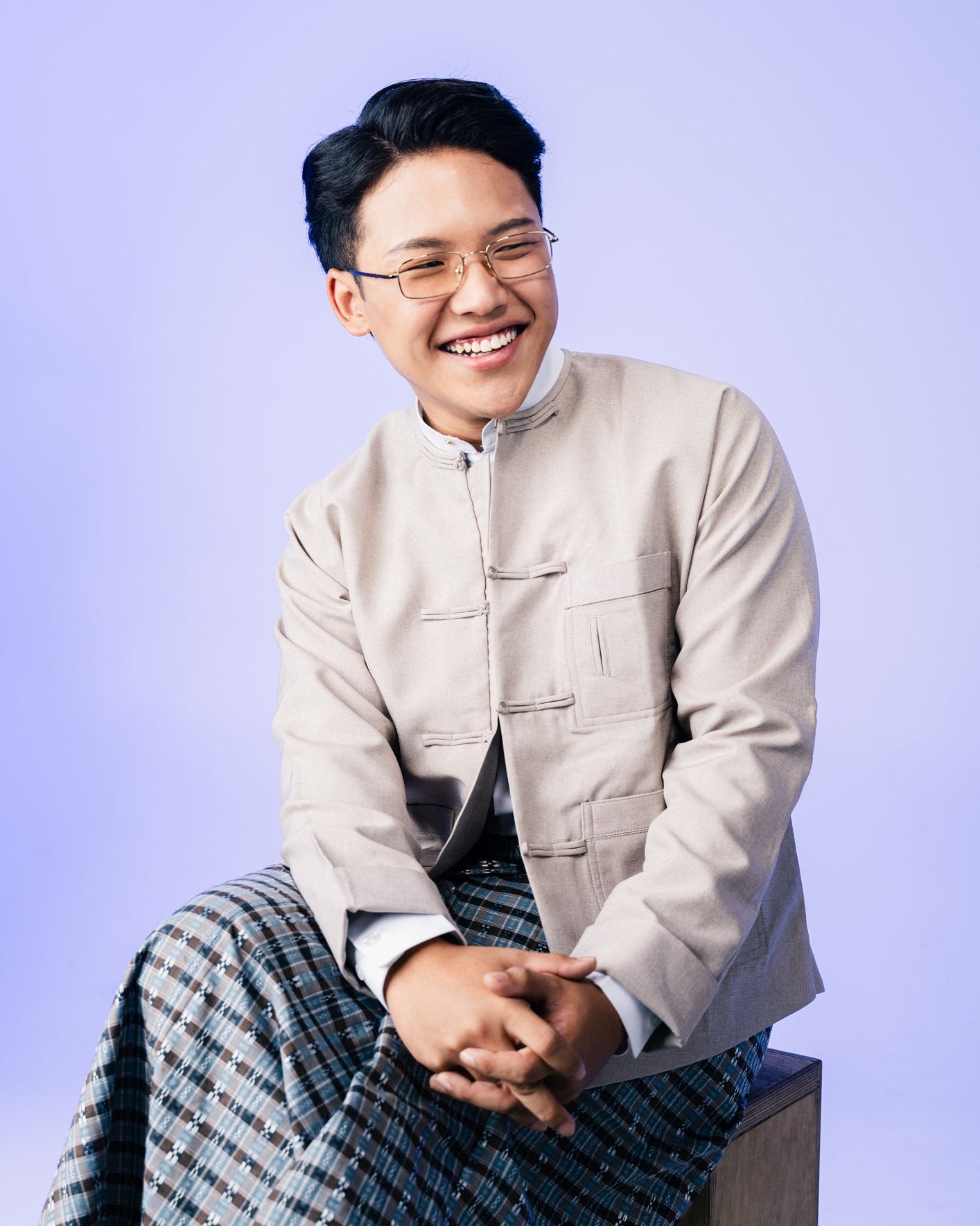 Person wearing a light-colored jacket and patterned pants against a purple background